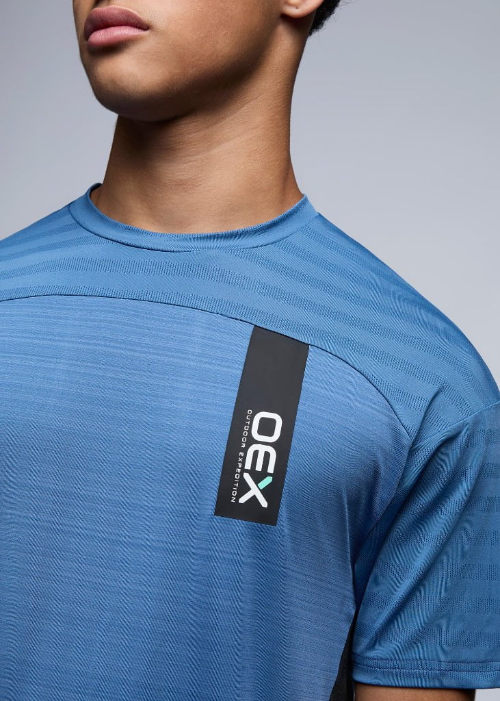Blue athletic shirt with a visible brand logo on a gray background
