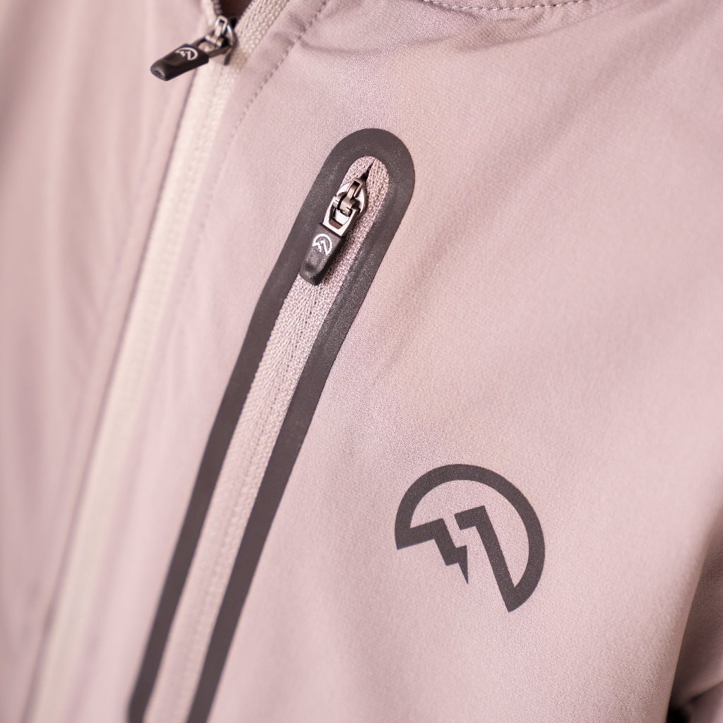 Close-up of a light pink jacket with a zipper and logo on a light background