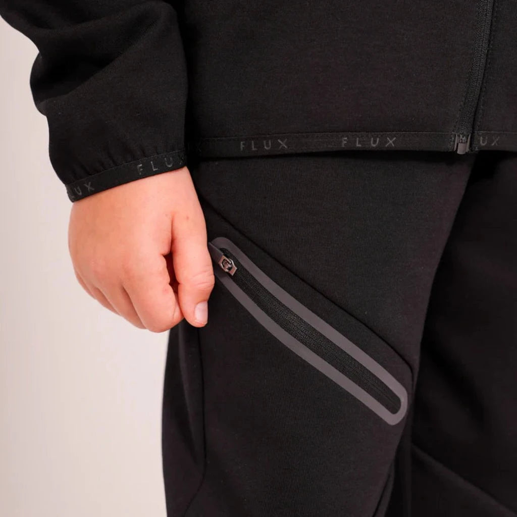 Person wearing a black jacket with a visible brand logo on a plain background